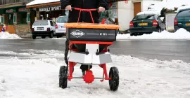 Carretilla distribuidora de empuje K51 con sal y arena en acción en invierno en la nieve