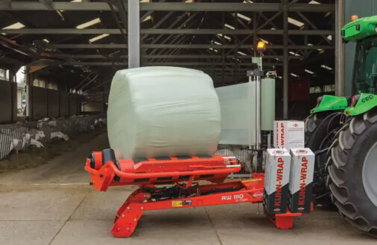 La RW 1110 encintando una paca redonda frente a un establo de cabras.