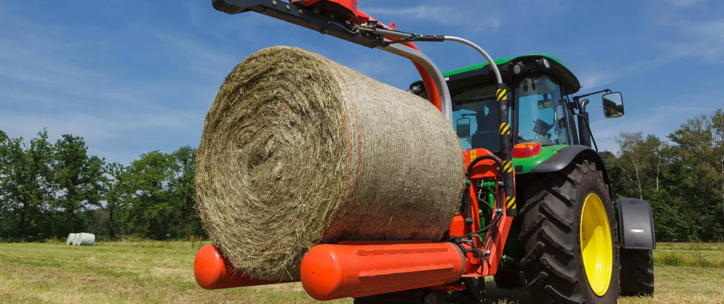 La encintadora de pacas suspendida en 3 puntos RW 1200 coge una paca para encintarla.