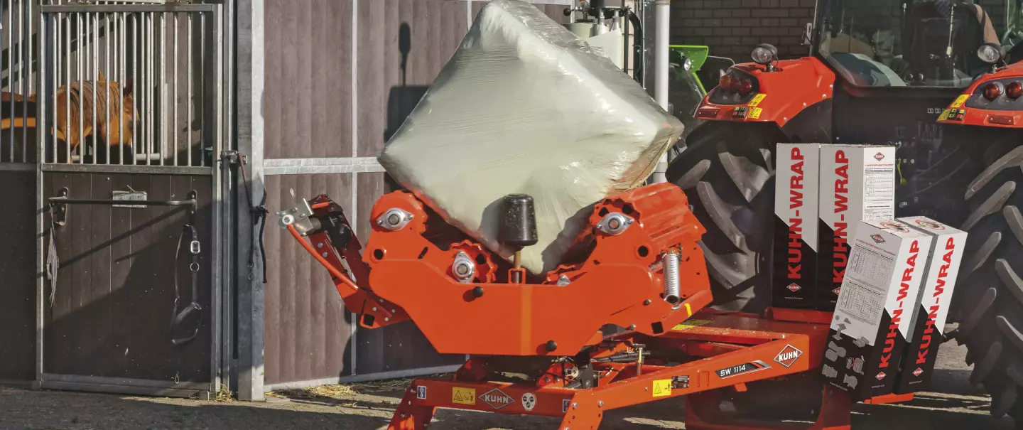 Una encintadora de pacas cuadradas SW 1114, encintando de forma fija frente a un establo de caballos.